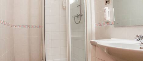 Un baño con ducha de vidrio, lavamanos con espejo y paredes de azulejos.