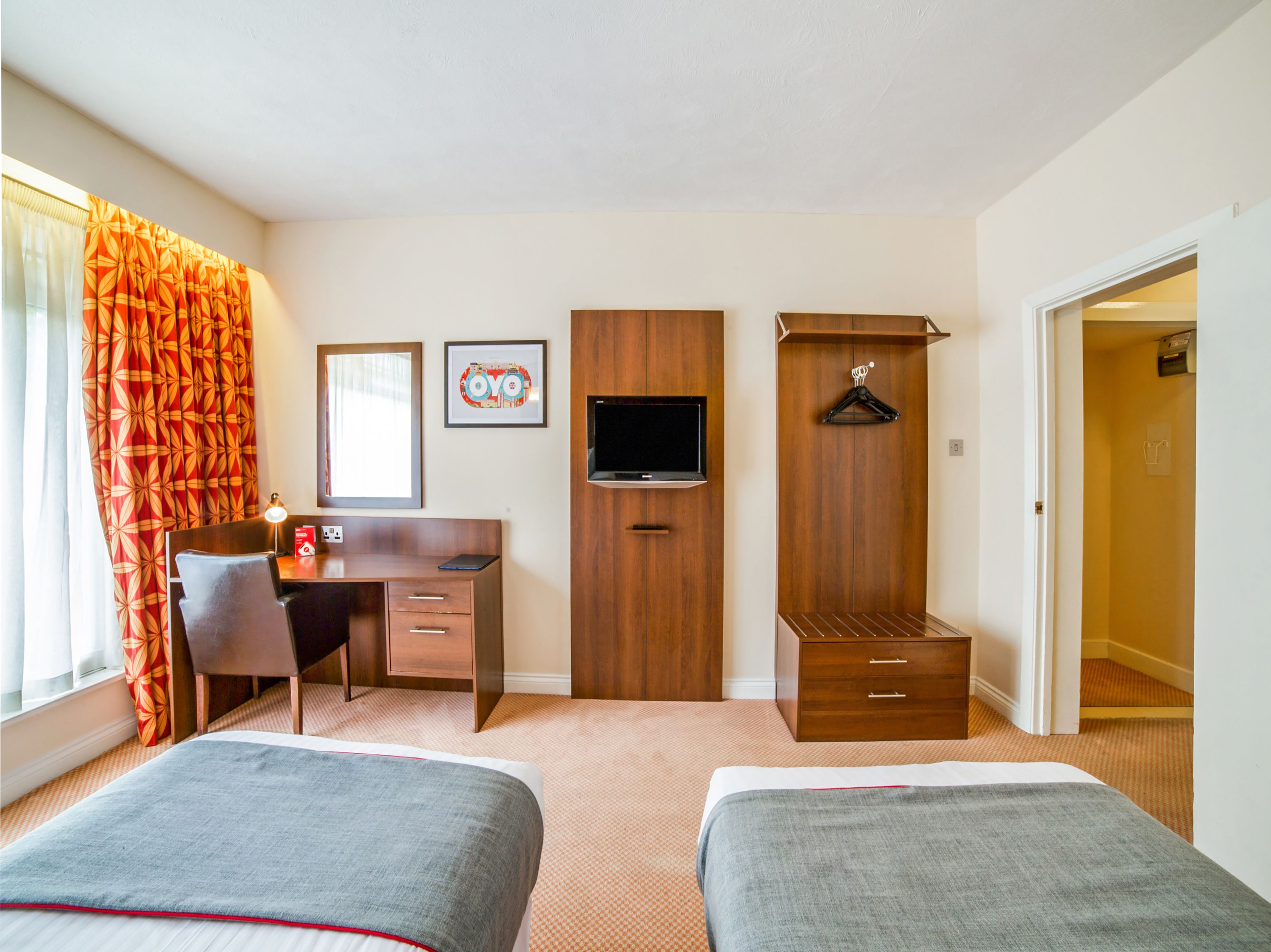 A hotel room with two beds, a desk, a TV, and a wardrobe.