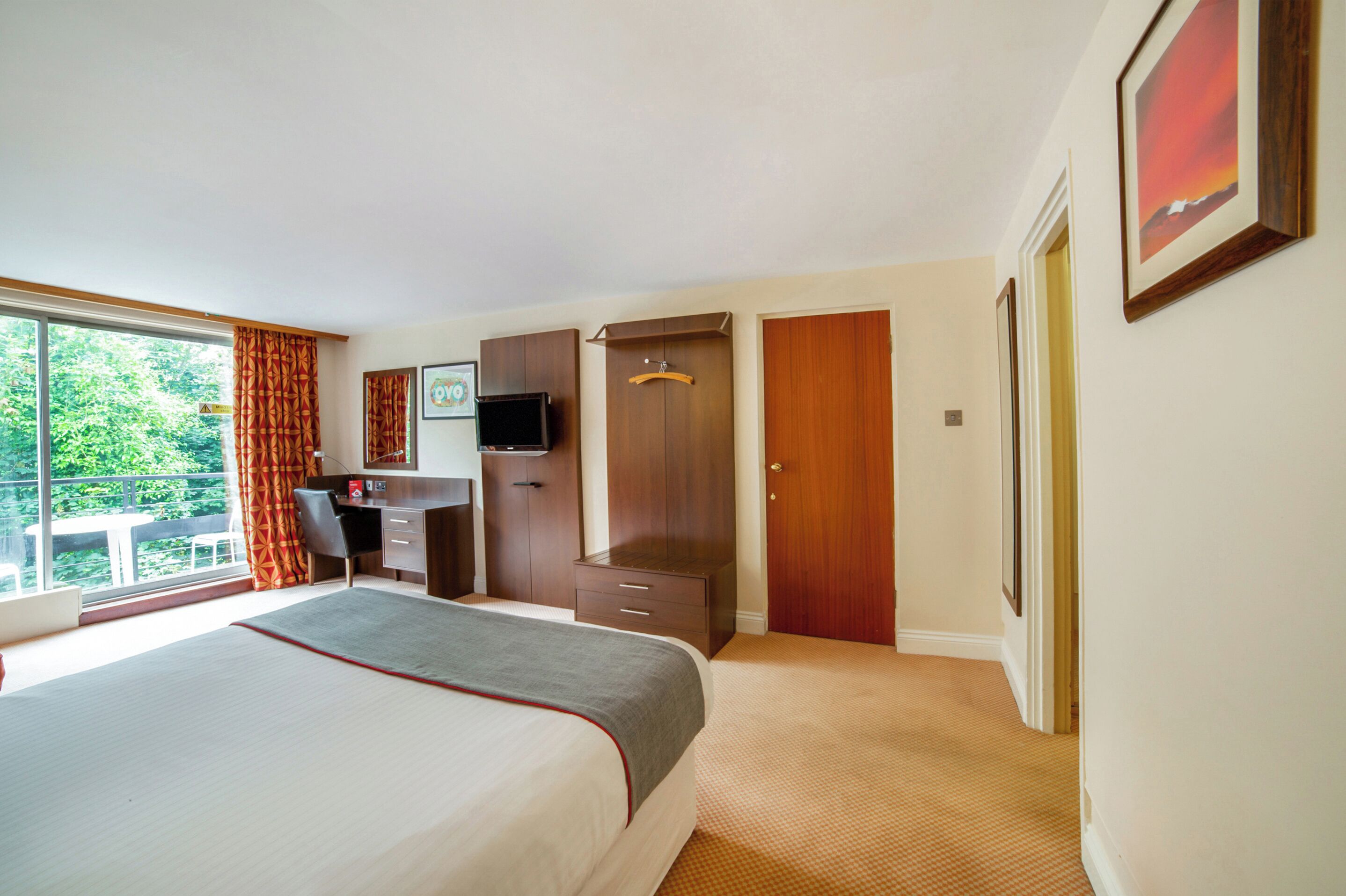Una habitación de hotel con cama, escritorio, armario y televisor.