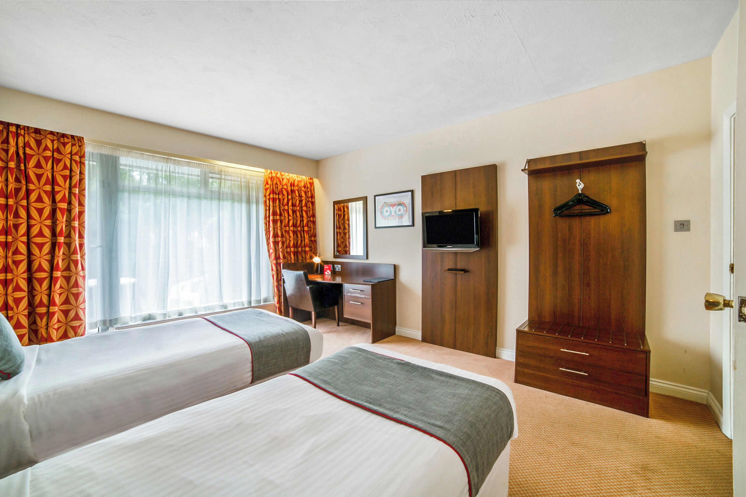 A hotel room with two beds, a desk, a television, and a wardrobe.