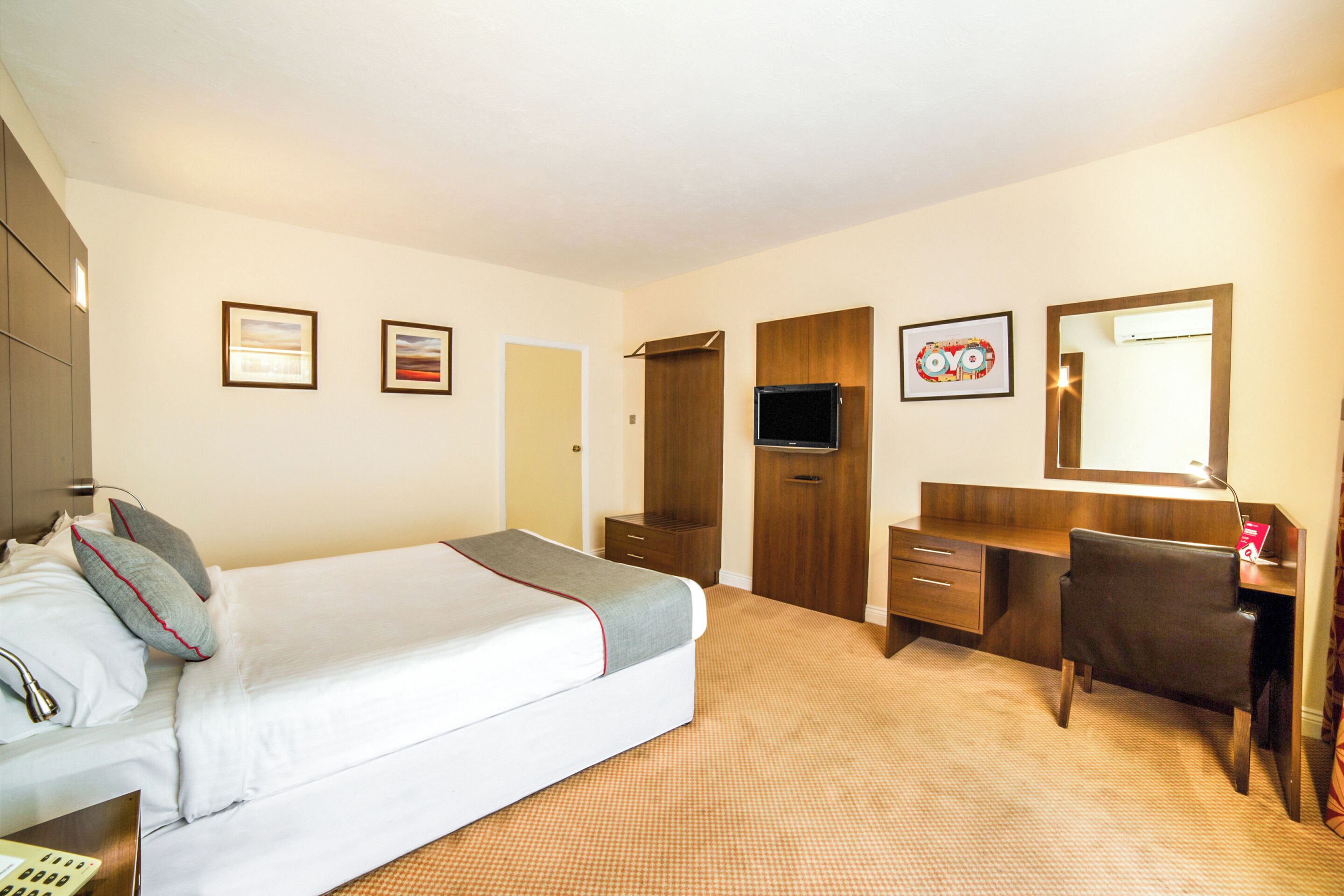 A hotel room with a bed, a desk, a chair, a TV, and a mirror.