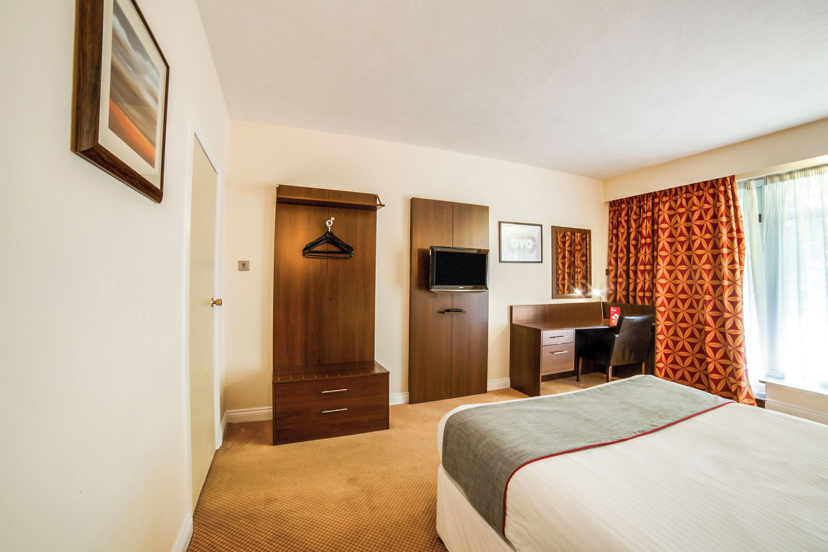 Una habitación de hotel con cama, escritorio, silla, armario y televisor.
