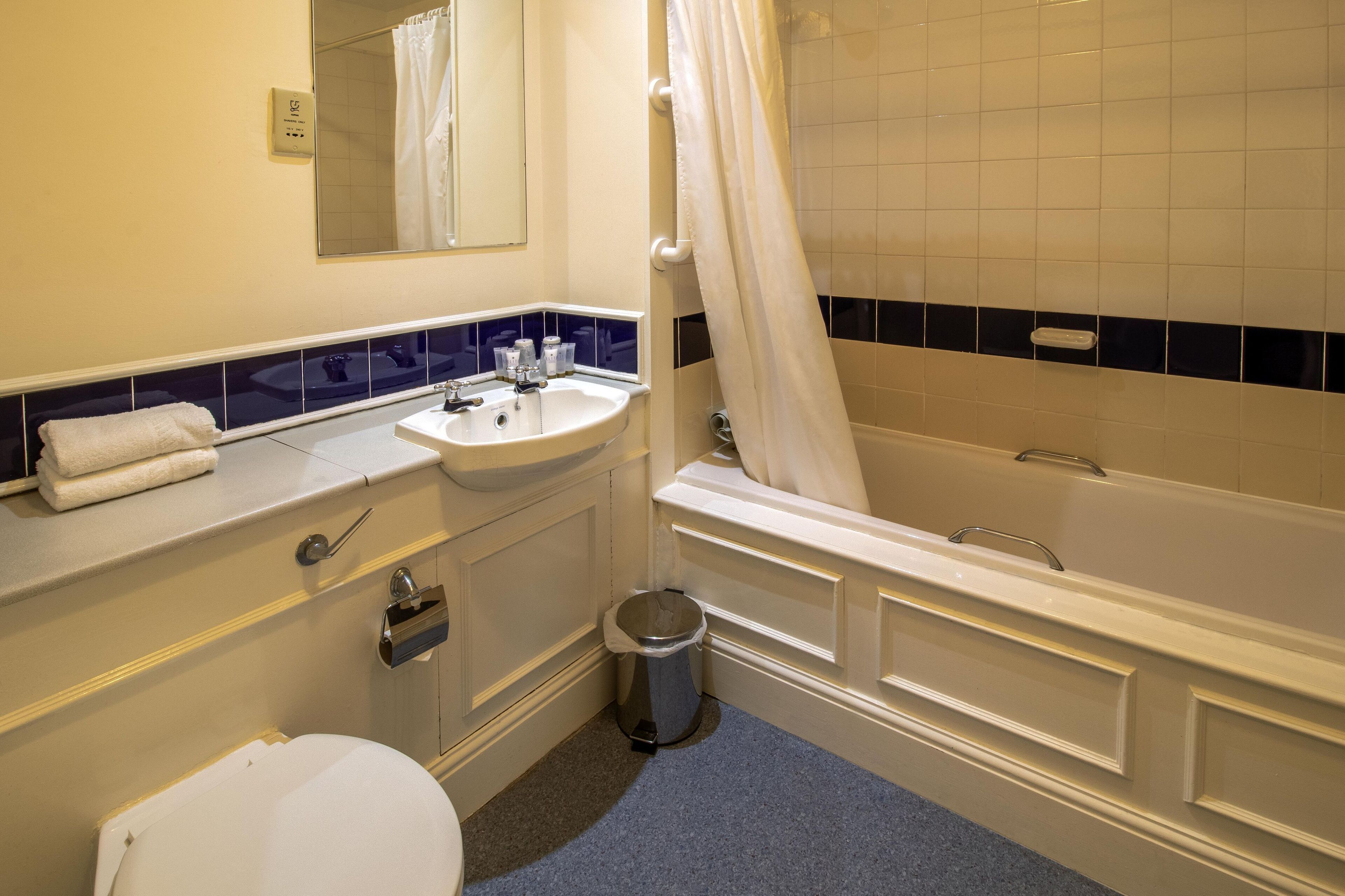 A bathroom with a white sink, mirror, and bathtub. There is a trash can and a towel on the counter.
