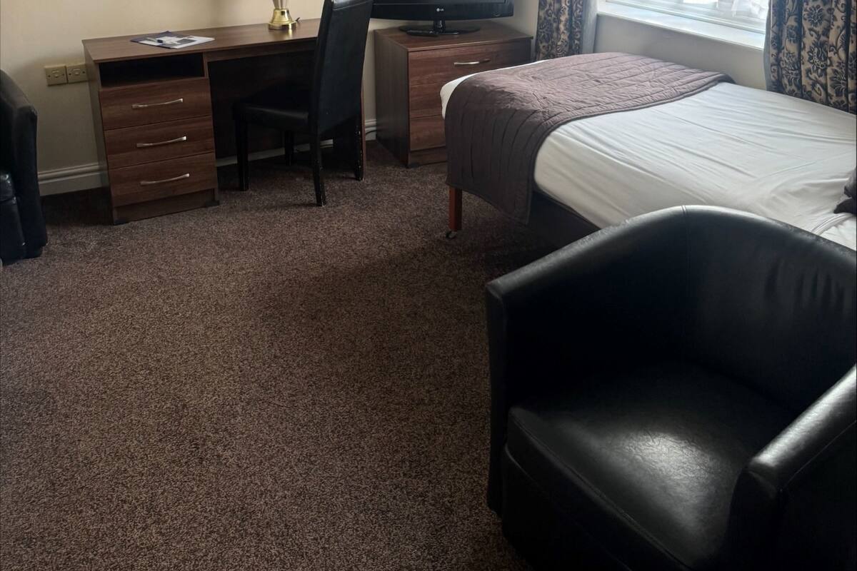 A hotel room with a bed, a desk with a computer, a chair, a TV, and a window with curtains.