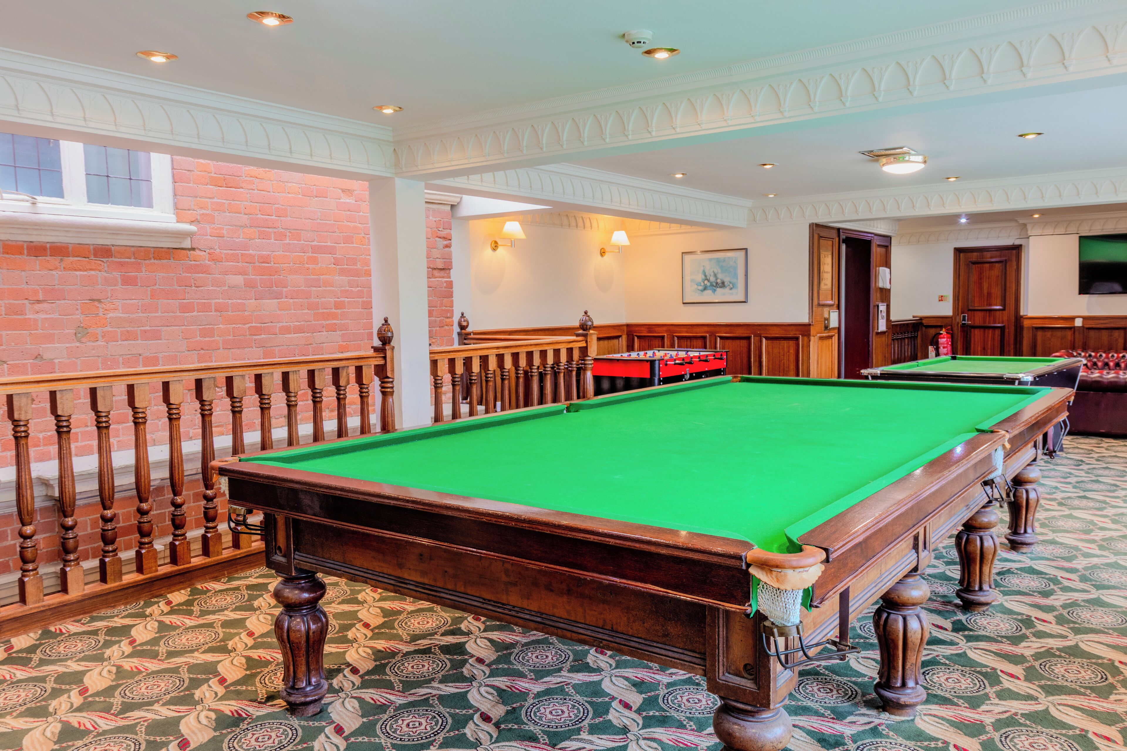 A pool table in a room with patterned carpet, brick walls, and wooden railings.