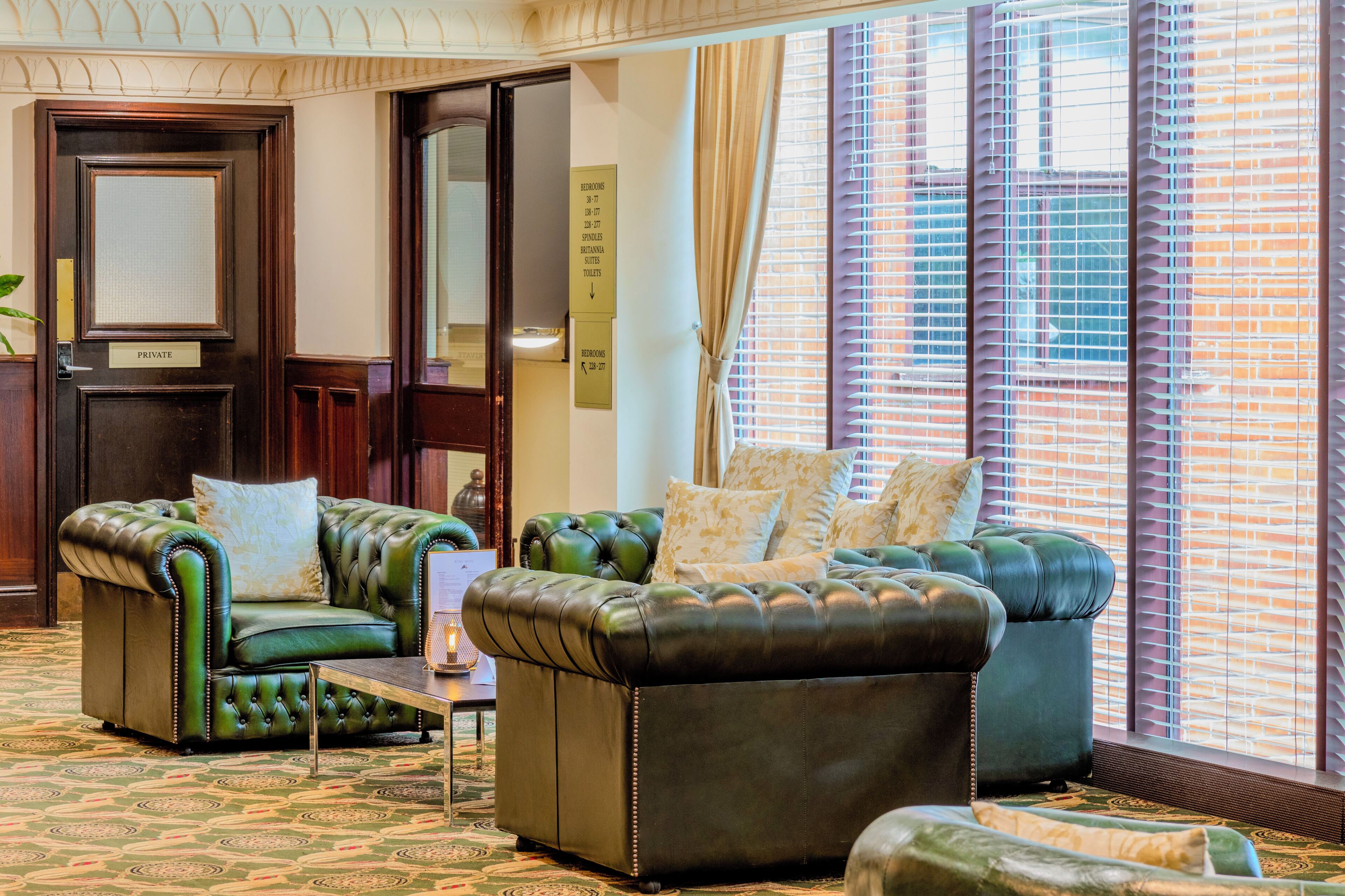 A room with a green leather sofa set, a small table, and a patterned carpet.