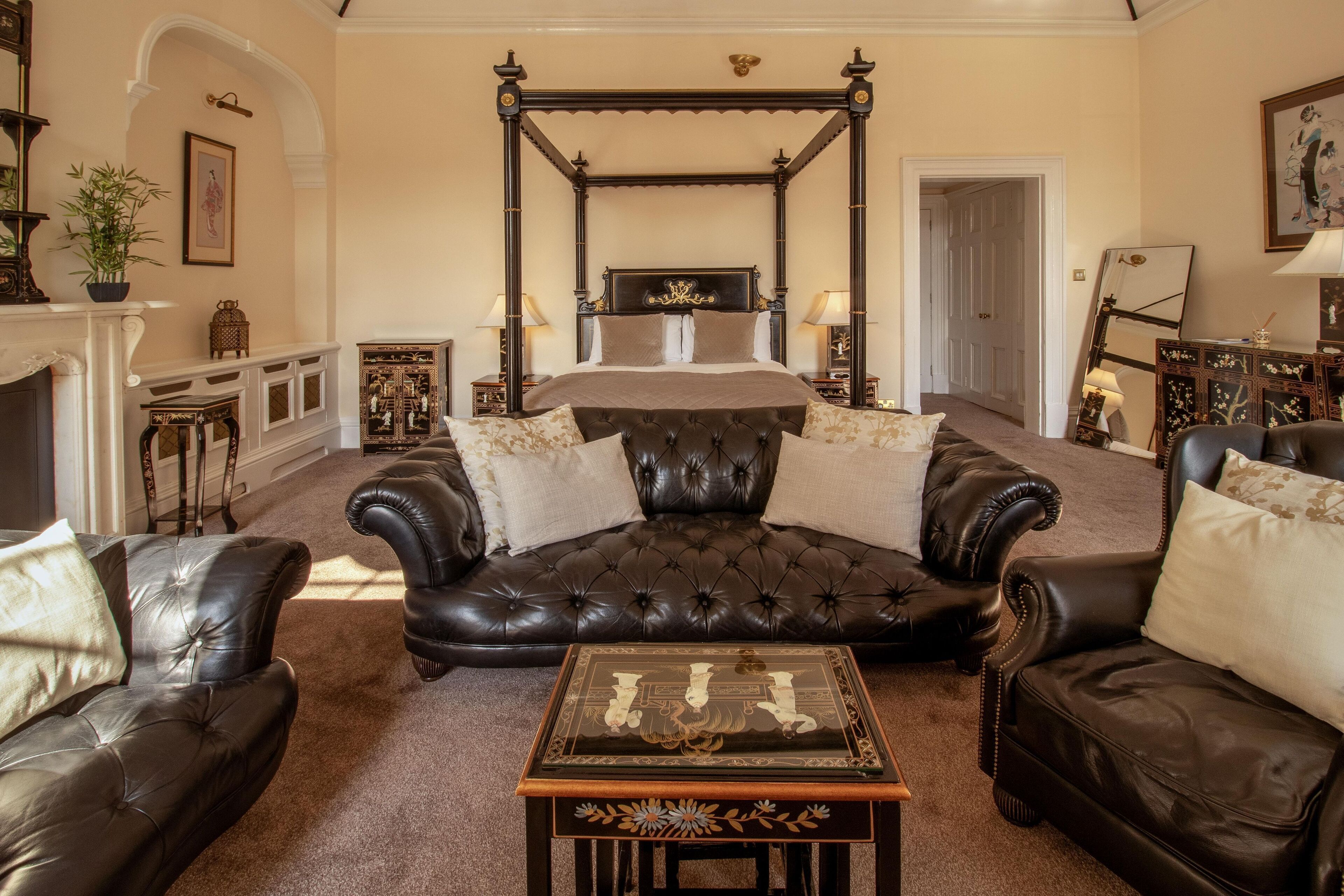 A bedroom with a four-poster bed, leather sofas, and a decorative table.