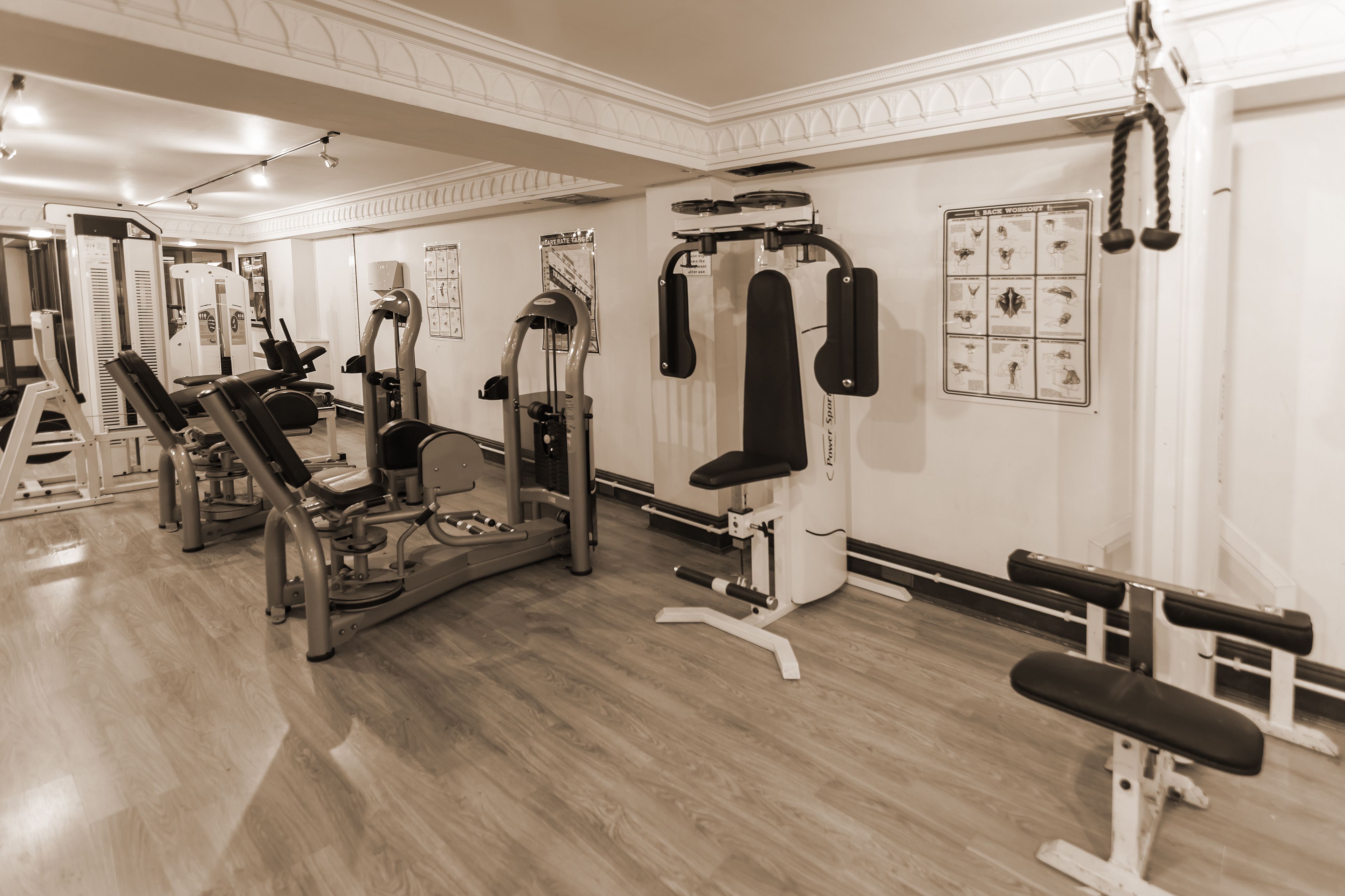 Un gimnasio con diferentes máquinas de ejercicio, una banca y una pared con carteles de fitness.
