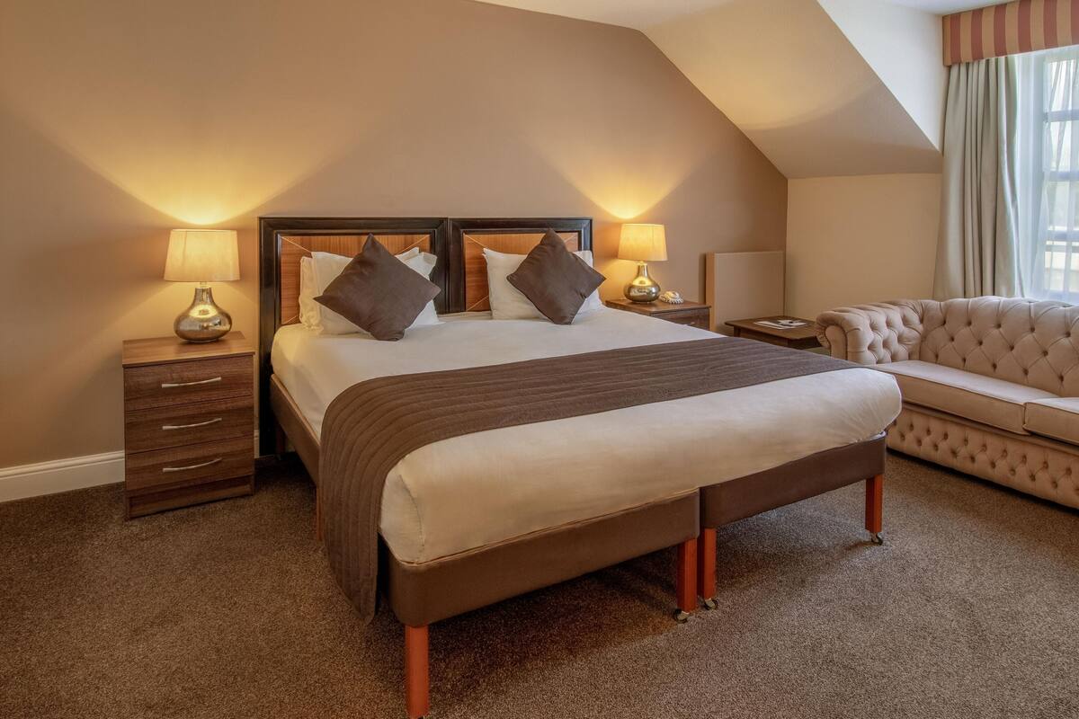 A hotel room with a large bed, two bedside tables with lamps, a sofa, and a carpeted floor.