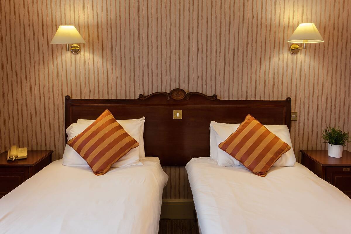 A double bed with striped pillows, a wooden headboard, and two wall-mounted lamps.