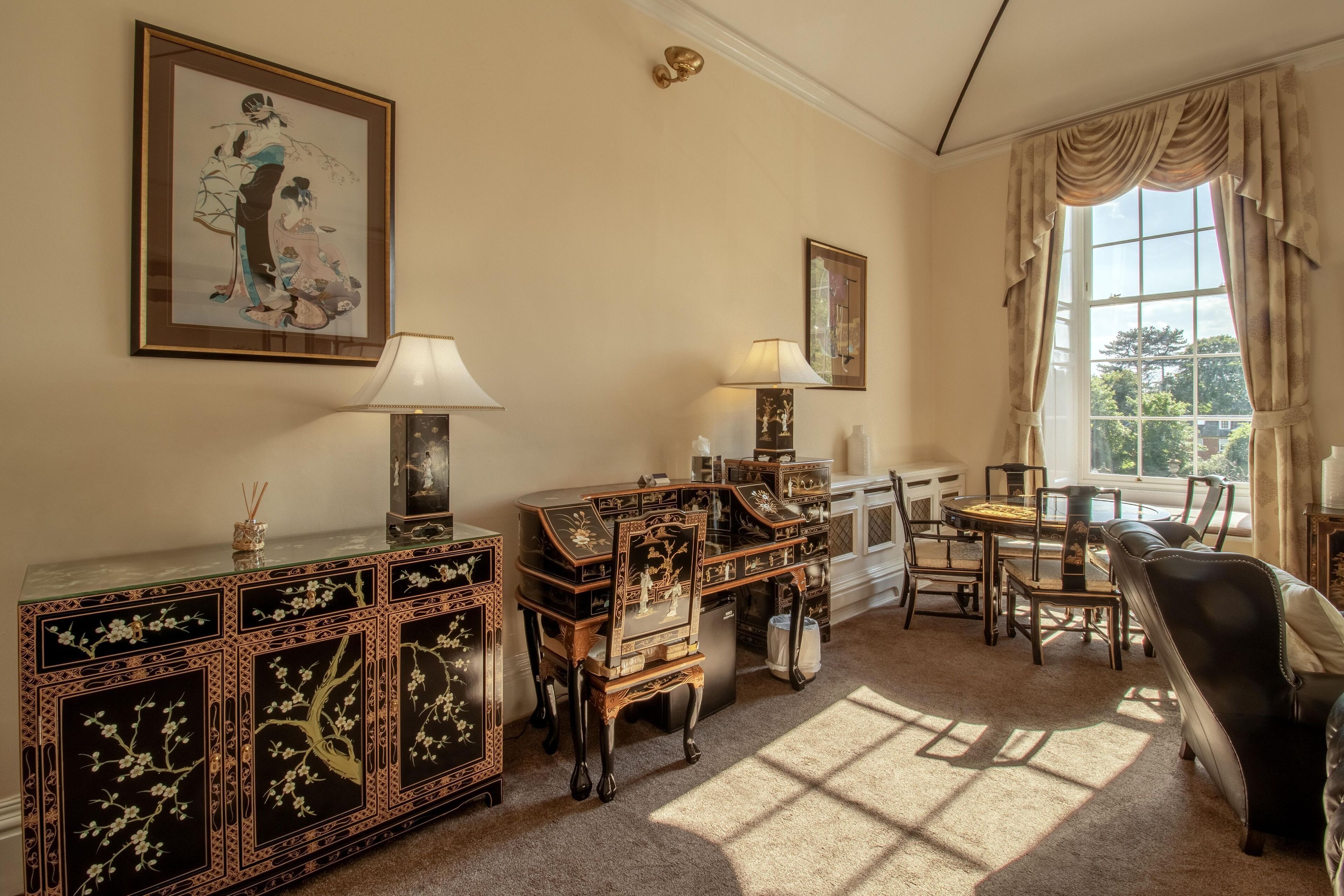A traditional room with a large window, a sofa, a cabinet with intricate designs, and a dining table with chairs.