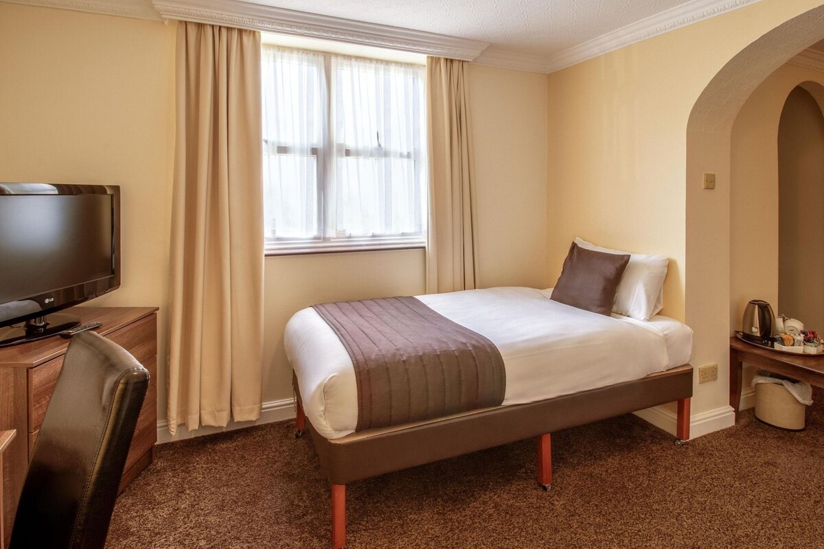 A hotel room with a bed, a television, a desk, and a window with curtains.