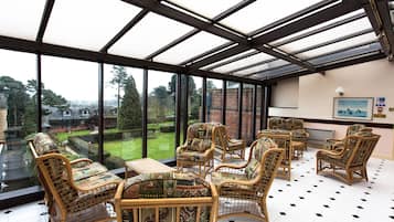A conservatory with wicker furniture and a view of a garden.