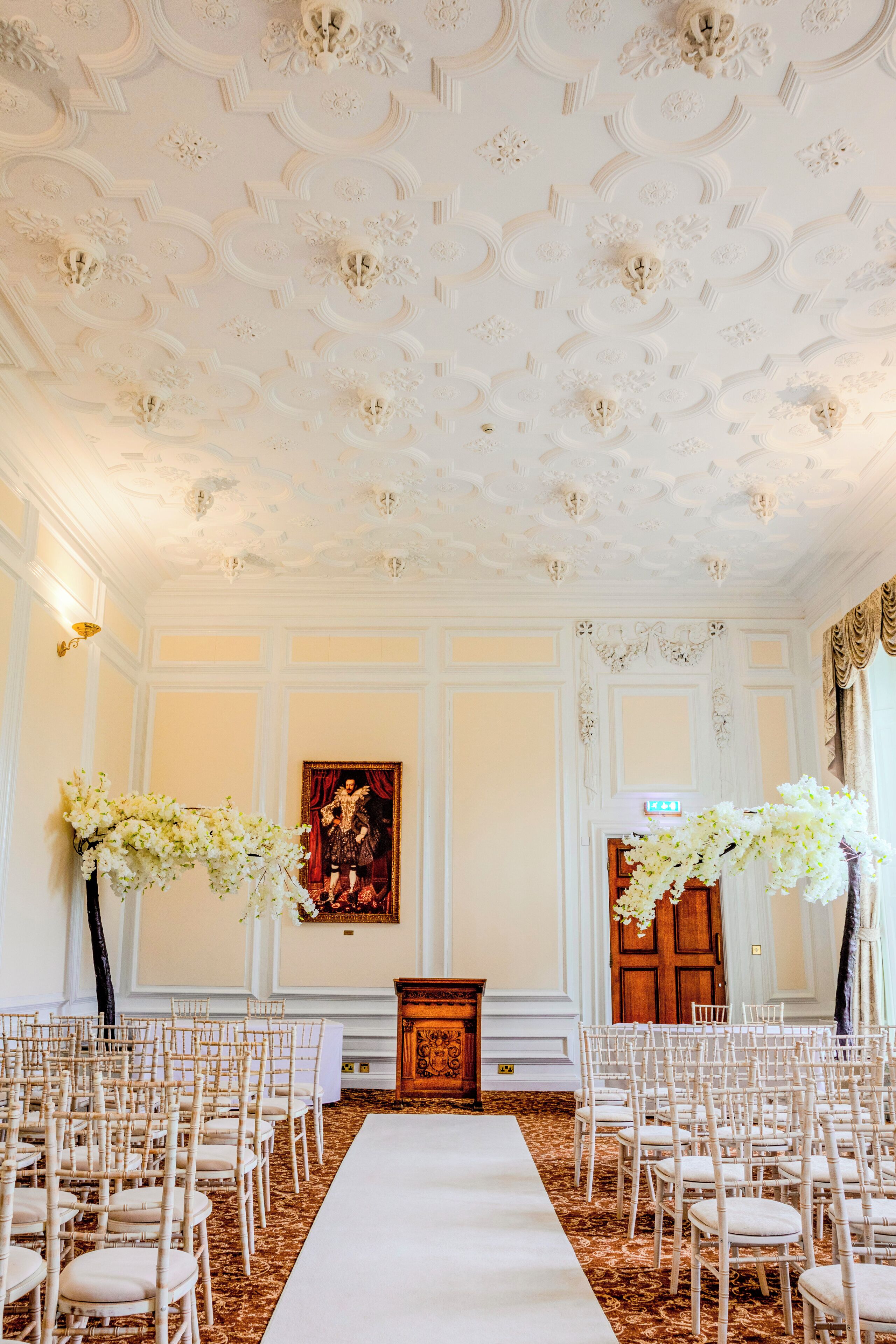 Une salle élégante avec une allée recouverte d’un tapis blanc, des chaises blanches et un pupitre en bois.
