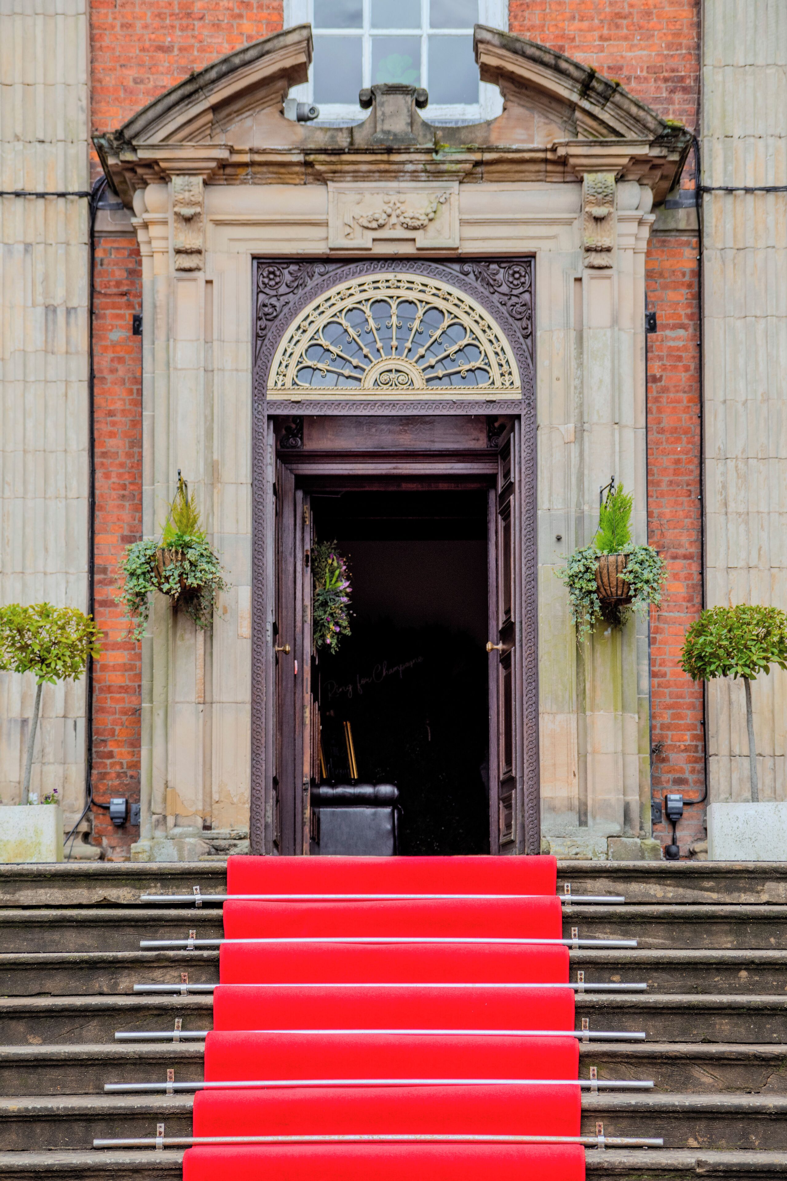 A grand entrance with a large arched doorway, steps leading up to it, and two potted plants on either side.