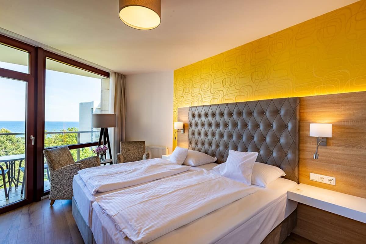A hotel room with a large bed, a view of the sea, and a balcony with a chair.