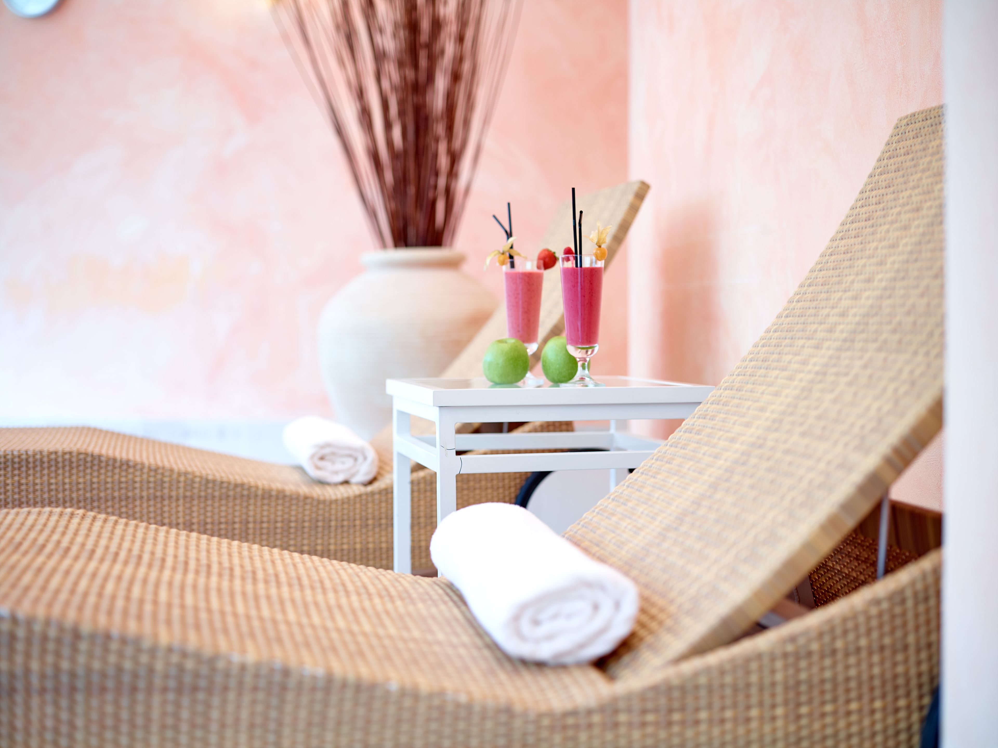 Ein Zimmer mit zwei Korbsesseln, einem kleinen weißen Tisch mit zwei Getränken und einem zusammengerollten Handtuch.