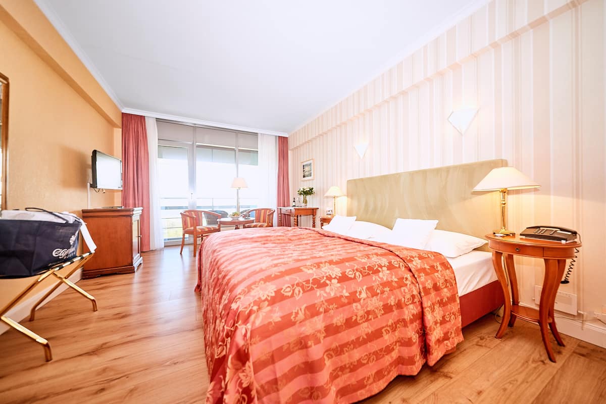 A hotel room with a bed, bedside table, lamp, and a desk with a chair.