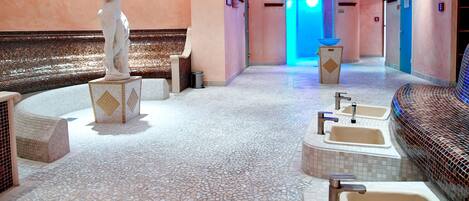 A modern spa area with a mosaic floor, seating, and a statue.