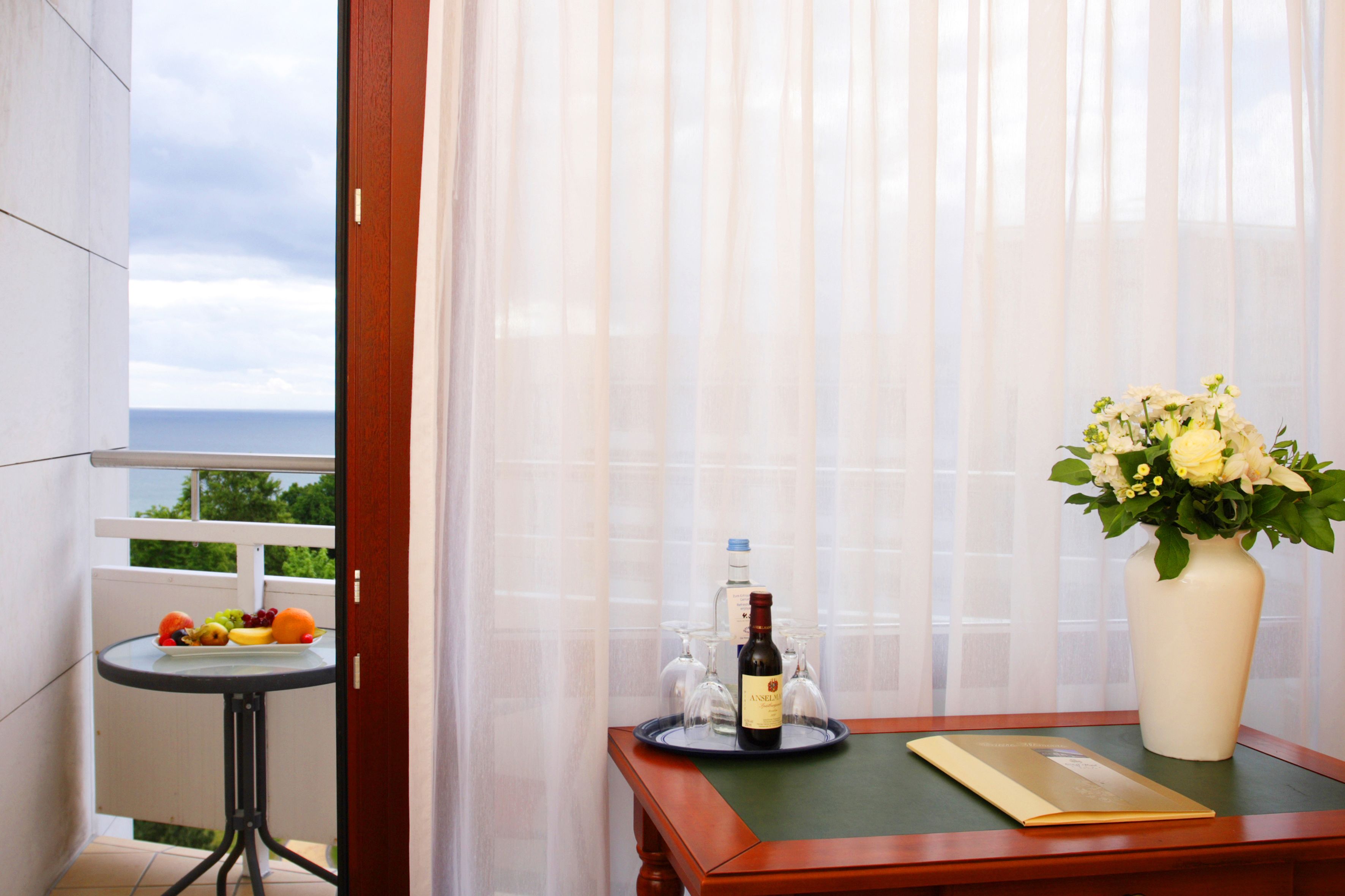 Een balkon met een tafel, een bloevas, een fles wijn en een dienblad met glazen en fruit.