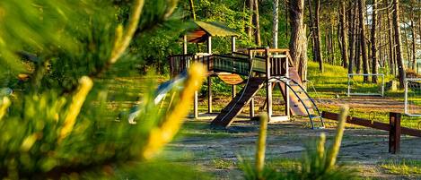A playground with a slide and climbing structure surrounded by trees.