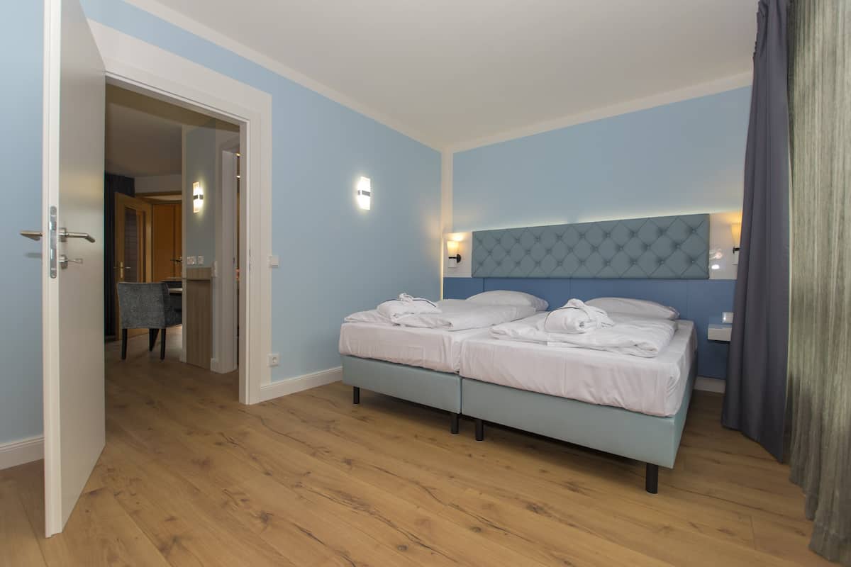 A bedroom with a double bed, a headboard, bedside lamps, and a wooden floor.