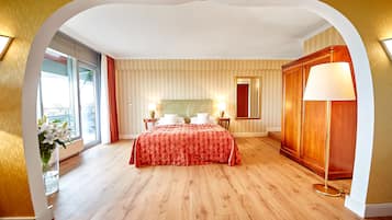 Habitación de hotel con una cama grande, un armario de madera, una mesita de noche con lámpara y una ventana con cortinas.