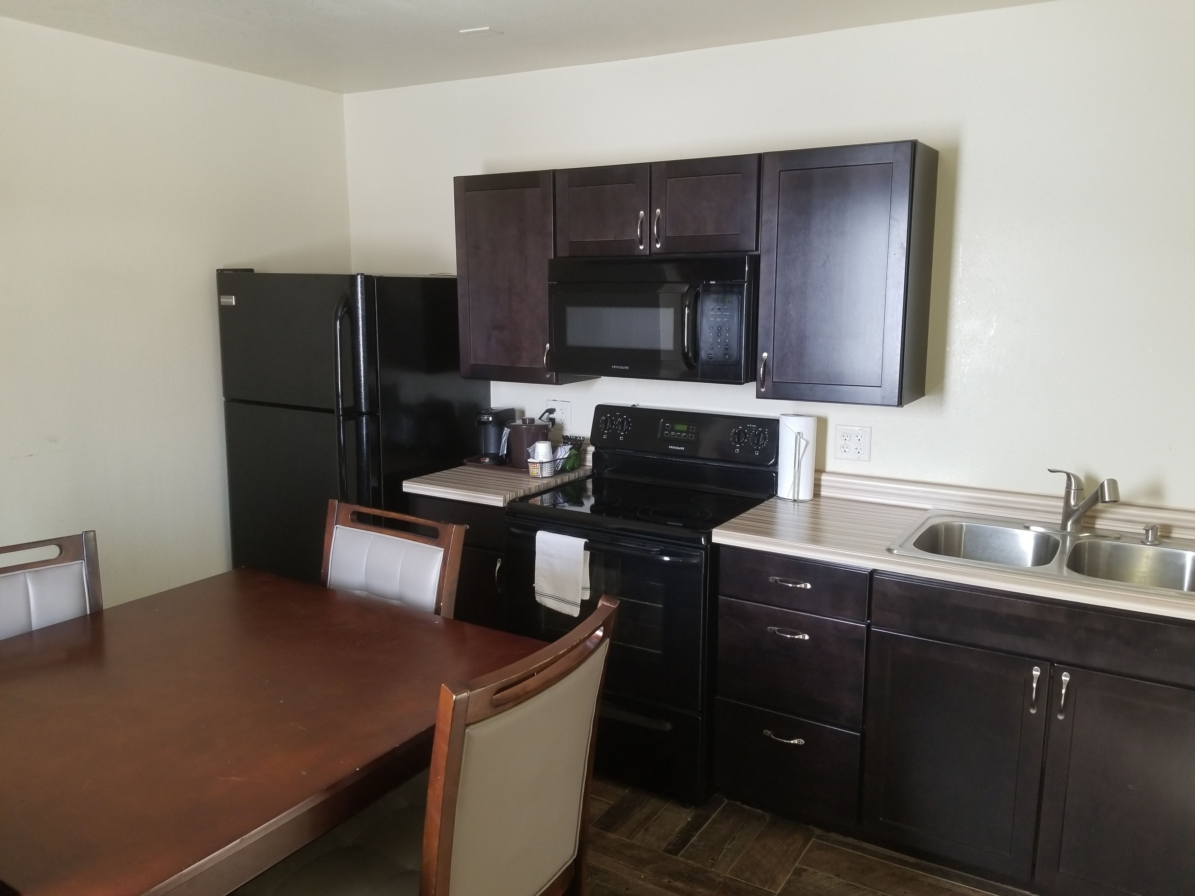 A compact kitchen with dark cabinetry, a refrigerator, a microwave, an oven, and a sink.