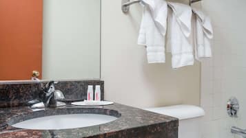 A bathroom with a granite sink, a mirror, a towel rack with towels, and toiletries on the counter.