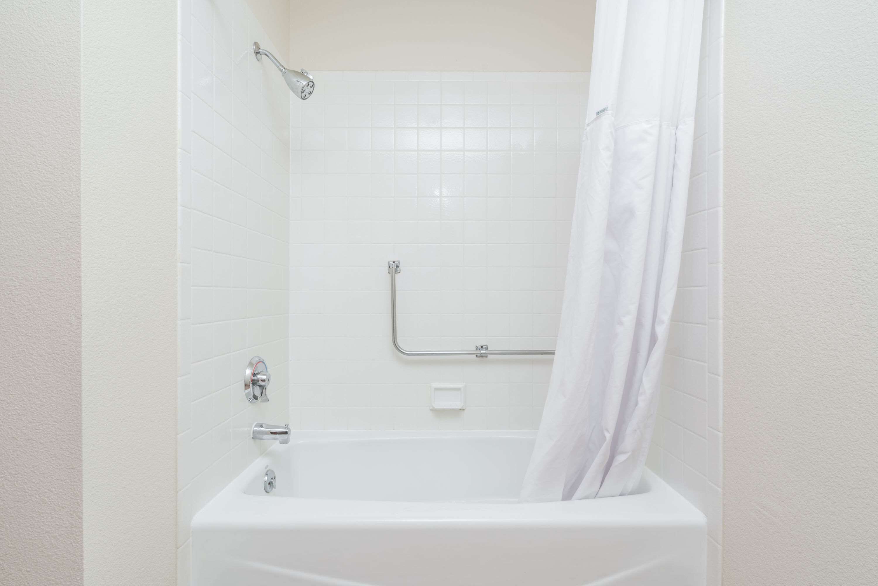 Une baignoire blanche avec un rideau de douche, une barre d’appui et une douchette à main.