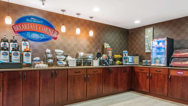 A breakfast counter with a Baymont sign, coffee machines, and various food items.