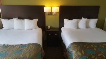 A hotel room with two beds, each with white linens and matching pillows. There is a nightstand with a lamp between the beds. The walls are painted yellow, and the floor is carpeted.
