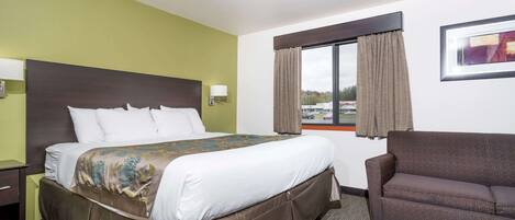 Habitación de hotel con una cama grande, un sofá, una ventana con cortinas e imagen enmarcada en la pared.