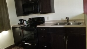 A compact kitchen with dark cabinetry, a microwave, an oven, and a sink.