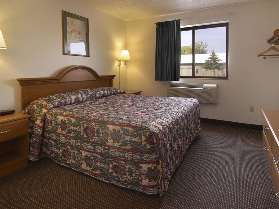 A hotel room with a bed, bedside lamps, a TV, a window with curtains, and an air conditioning unit.