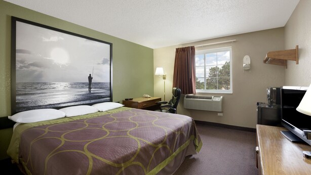Une chambre d’hôtel avec un grand lit, un bureau, une télévision, une fenêtre avec des rideaux et un climatiseur fixé au mur.