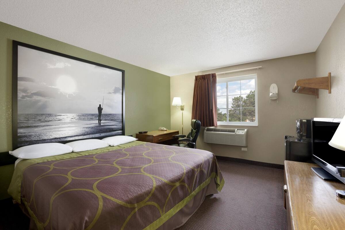 Una habitación de hotel con una cama grande, un escritorio, un televisor, una ventana con cortinas y un aire acondicionado de pared.