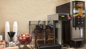Un coin café équipé d’une machine à café, de tasses et d’un panier de pommes.