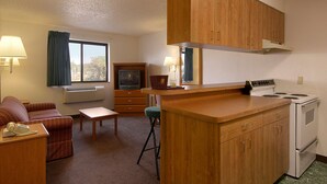 Une chambre d’hôtel compacte comprenant un coin cuisine, un canapé, une petite table et un téléviseur.