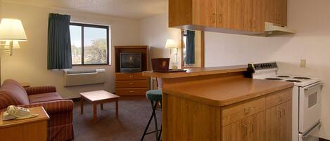 A compact hotel room with a kitchenette, a sofa, a small table, and a TV.