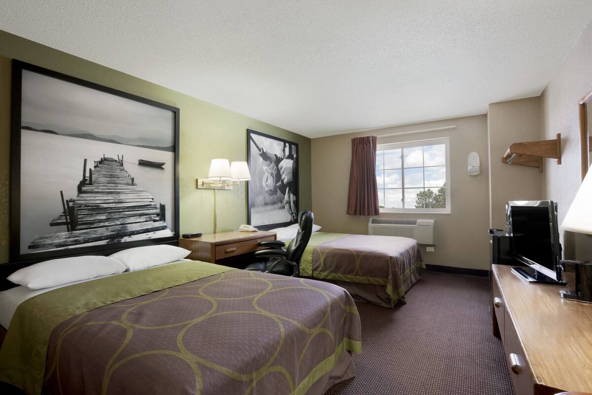 Habitación de hotel con dos camas, un escritorio con computadora, televisor y obras de arte en las paredes.