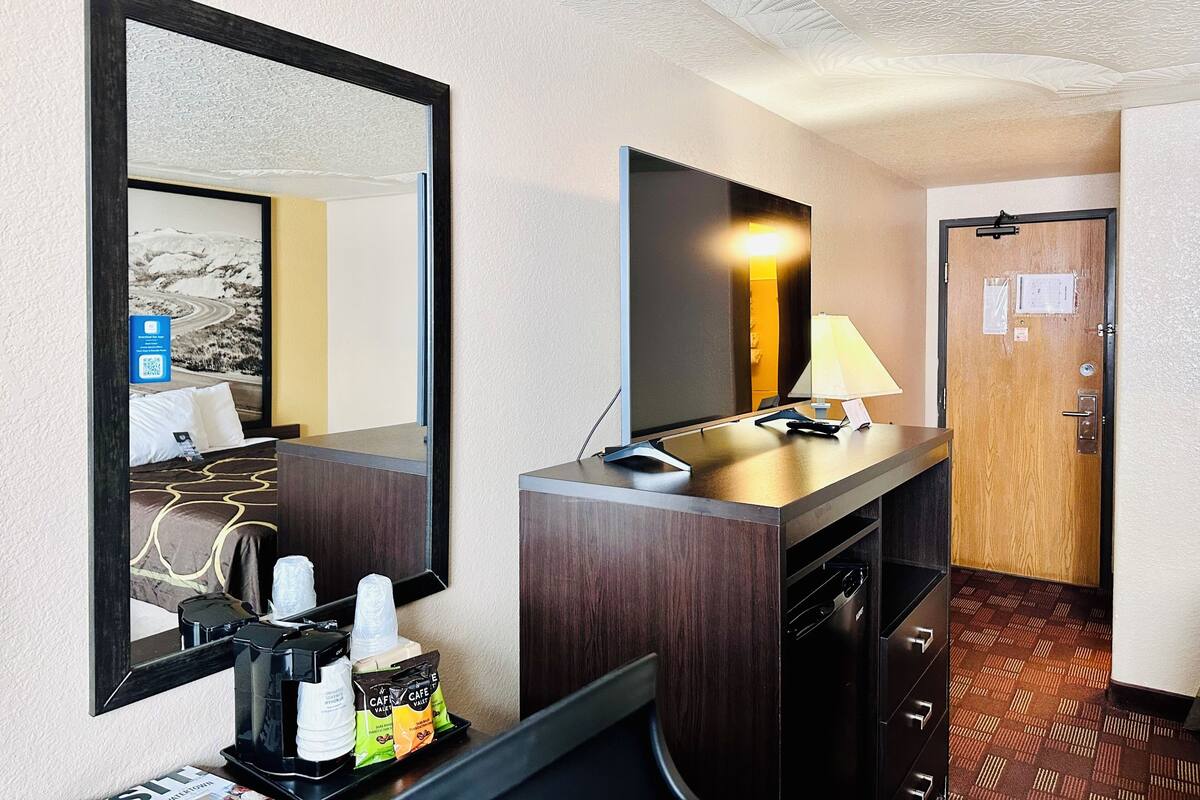 Une chambre d’hôtel dotée d’un grand miroir, d’un téléviseur à écran plat, d’un bureau avec une lampe, d’une machine à café et d’un mini-bar.