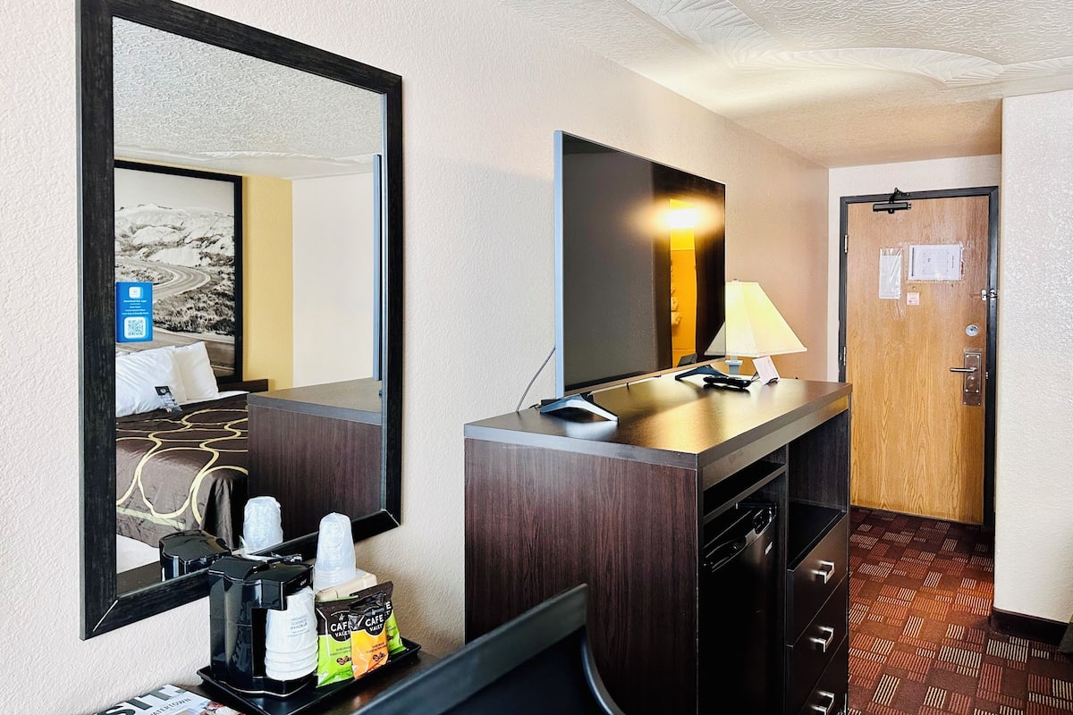 Une chambre d’hôtel dotée d’un grand miroir, d’un téléviseur à écran plat, d’un bureau avec une lampe, d’une machine à café et d’un mini-bar.