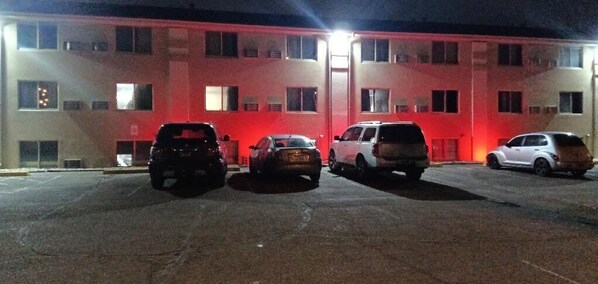 A parking lot with several cars parked in front of a building with multiple windows and a red-lit facade.