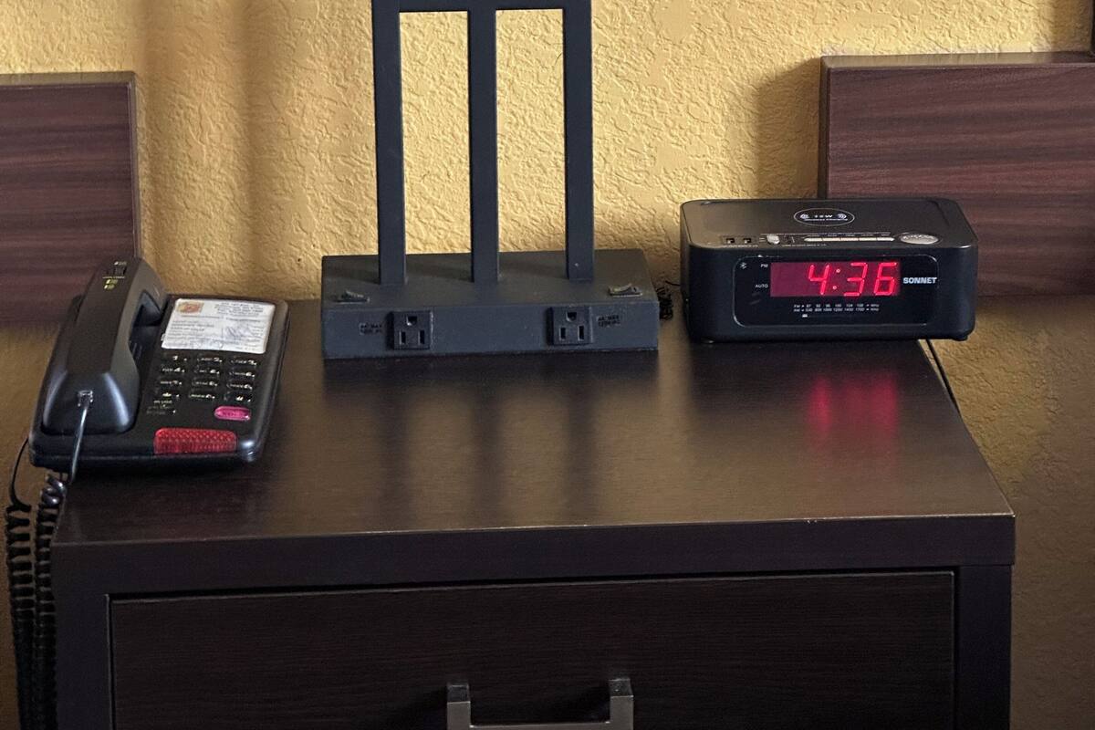Une table de chevet avec une lampe, un téléphone et un réveil numérique affichant 4h36.
