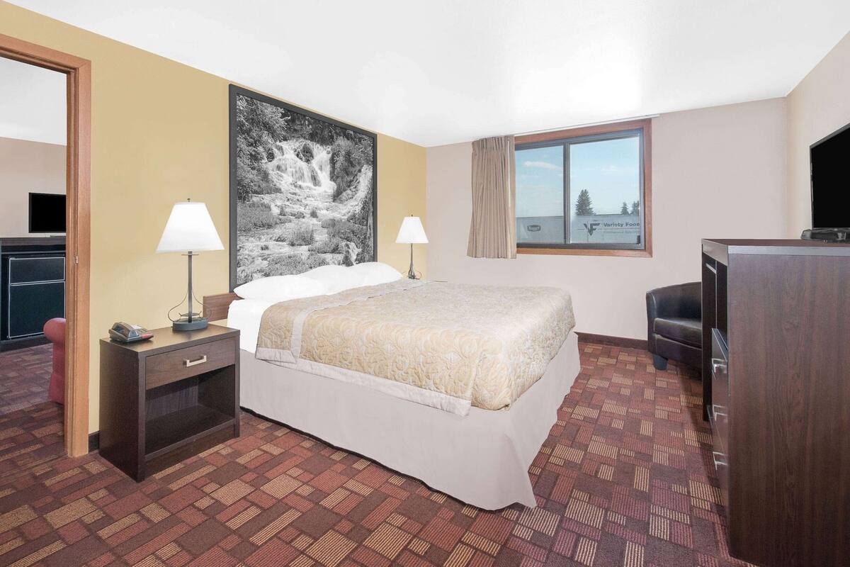Une chambre d’hôtel comprenant un lit, deux lampes de chevet, un bureau avec un téléphone, une grande fenêtre donnant sur un beau paysage et un téléviseur.