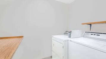 Een wasserette met een wasmachine en droger, een houten plank en een schuine kap.