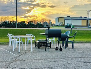 An outdoor seating area with a grill and chairs, a parking lot, and a building in the background. - Super 8 by Wyndham Watertown (Watertown)