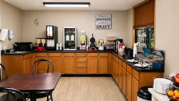 Una cocina con una mesa de comedor, sillas, microondas, cafetera, refrigerador y un cartel en la pared.