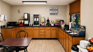 Una cocina con una mesa de comedor, sillas, microondas, cafetera, refrigerador y un cartel en la pared.